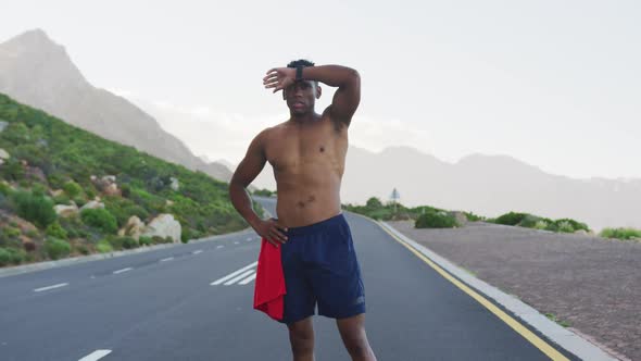 African american man standing and flexing his muscles on a coastal road alt