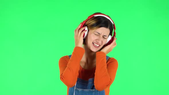 Cheerful Girl Dancing and Enjoys Music in Big Red Headphones. Green Screen alt