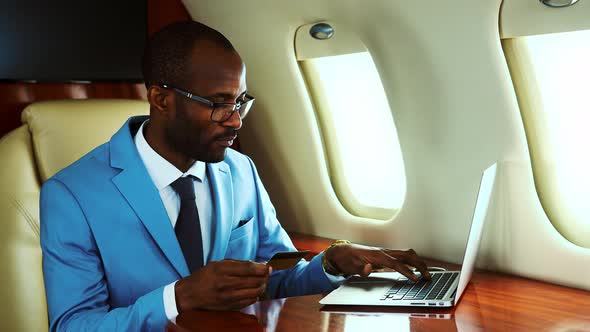 Businessman making online payment on airplane with credit card alt