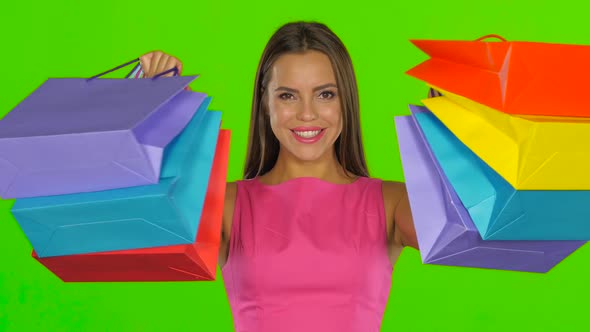 Woman Joyfully Looks Out From Behind Shopping Bags. Green Screen. Close Up alt
