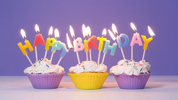 Happy Birthday Inscription Made of Burning Colorful Candles on Tasty Cupcakes Isolated on Purple