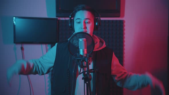 A Man in Hoodie Rapping in the Record Studio Gesticulates While Recording His Track alt