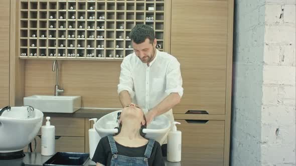 Handsome Hairdresser Washing Female Hair with Concentration. He Is Holding a Water Tap. Woman alt