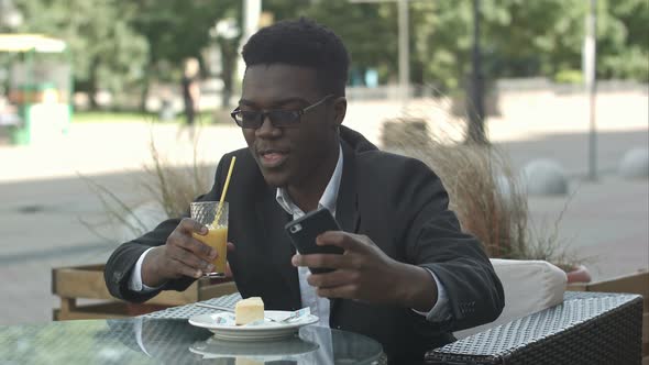 Smiling Young Businessman Sitting at Coffee Shop Using Mobile Phone, Taking Selfie alt