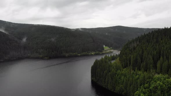 Rainy day, cloudy sky above a beautiful lake surrounded by pines. Pine forest around a narrow lake. alt