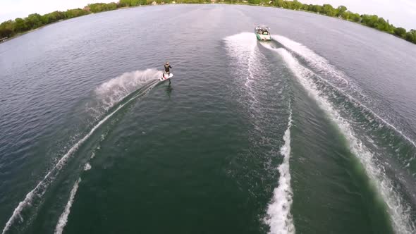 Aerial birds-eye drone view of a man wakeboarding behind a boat. alt