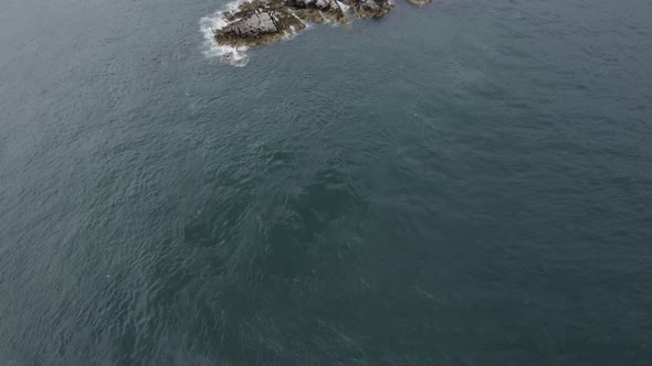 An aerial revealing capture of The Muglins Lighthouse during a cloudy day. alt