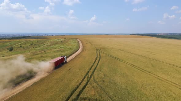 Aerial View of Cargo Truck Driving on Dirt Road Between Agricultural Wheat Fields Making Lot of Dust alt