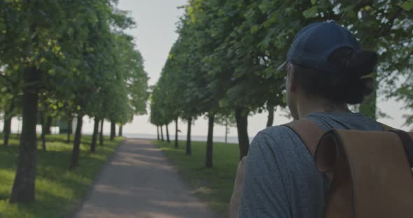 Lonely Traveler with a Backpack Walks Along the Path in the Park By the Sea alt