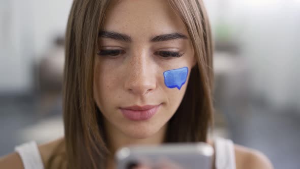 Portrait of Young Pleasant Woman Sitting at Home Using Her Mobile Phone and Smiling alt