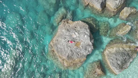 Aerial View of the Woman Laying Down at the Rock in the Clear Blue Sea alt
