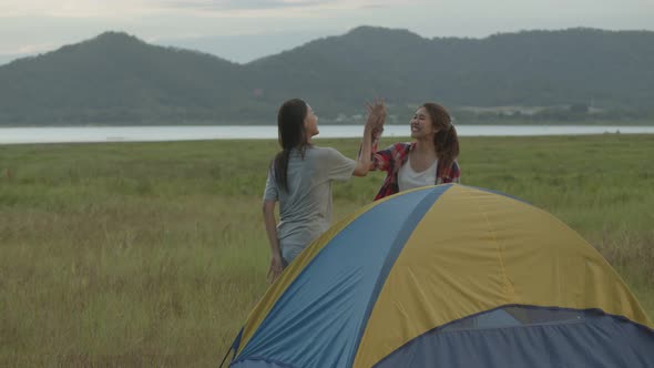 Asian women camping pitch a tent while sunset enjoying having fun together a summer traveling.