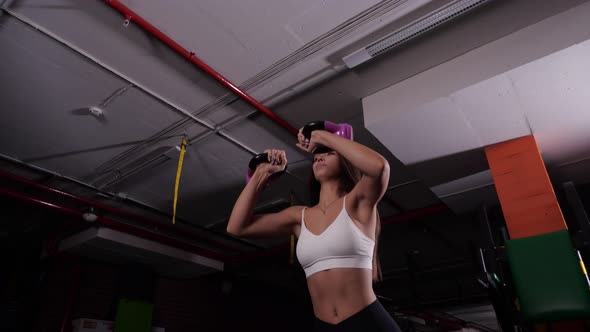 Attractive Girl in a White Sports Top Raises Dumbbells in the Gym alt