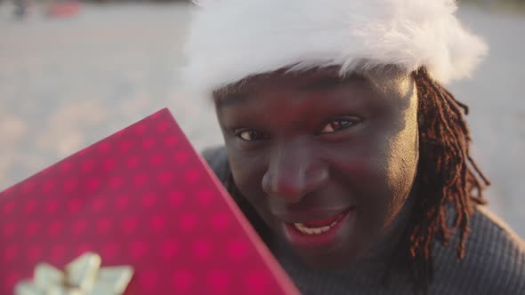Happy Black Man with Santa Hat Holding Red Wrapped Christmas Gift alt
