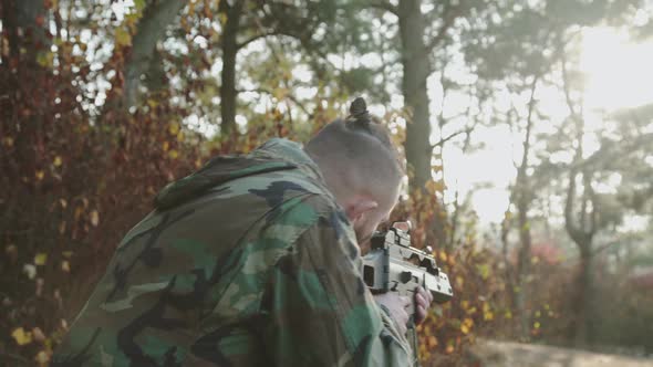 The Versatile View of Soldier Tracks the Object with a Rifle Sight at Forest alt