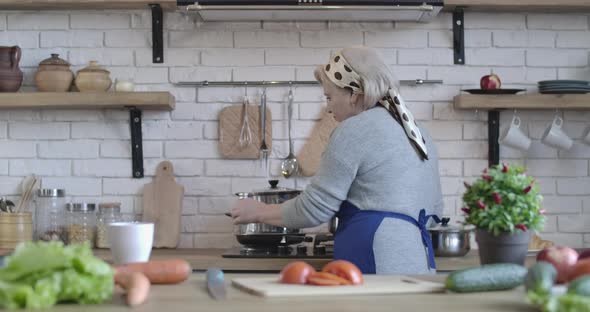 Serious Middle-aged Caucasian Woman Cooking Dinner on the Stove. Back Side View Portrait of Senior alt