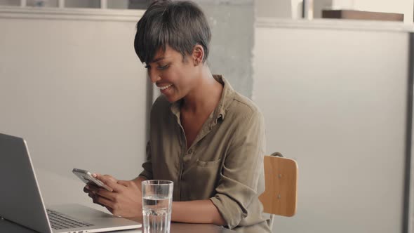 Mixed Race Black Woman in Front of Open Notebook Procrastinates with Smartphone