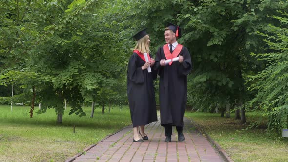 Young Happy Graduates Holding Diplomas and Walking in Park Talking and Relaxing alt