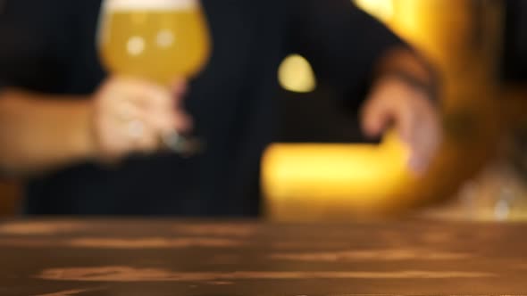 Close-up of a bartender moving a glass of fresh beer forward on the bar counter in a club