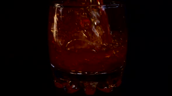 Pouring whiskey into a glass with ice on an isolated black background. Slow motion. alt