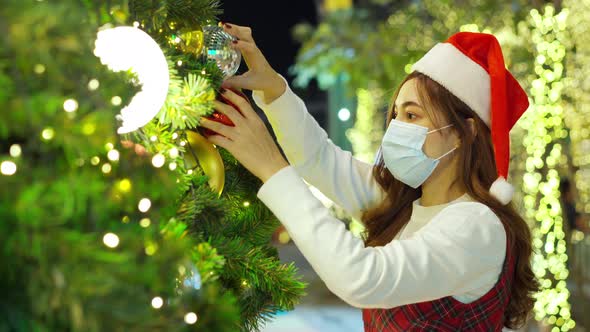 woman in medical mask and santa cap decorating Christmas tree
