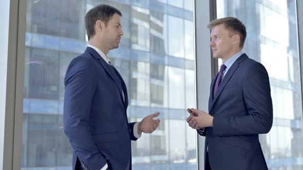 Two Middle Aged Businessmen Having Discussion Against Boardroom Office Window alt