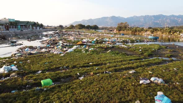 Coastal green grass near local Vietnam river covered in garbage, aerial view alt