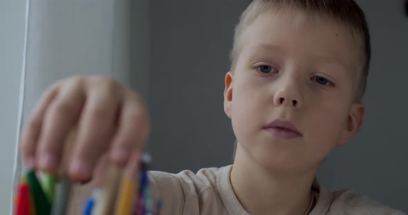 Front Portrait of Serious Kid Drawing Picture with Color Pencils at Table Slow Motion