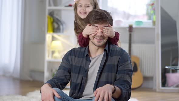 Playful Little Pretty Girl Closing Man's Eyes Playing Guess Who alt