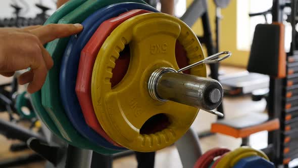Athlete Bodybuilder Counts the Weight of the Bar with Multicolored Discs on By Touching Each Disc