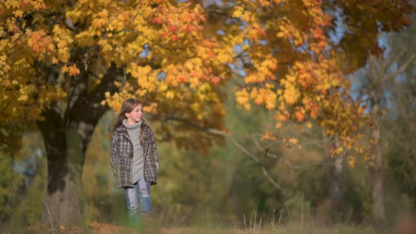 Happy Girl in Coat Walks in a Sunny Autumn Park.