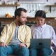 Happy Multiracial Young Couple Talking and Using Laptop Together Watching Video Sitting on Sofa in - VideoHive Item for Sale