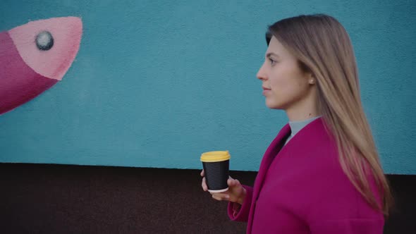 A Girl Walks Down the Street and Drinks Coffee