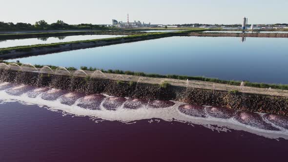 Aerial view of a red-colored wastewater reservoir near an industrial plant. alt