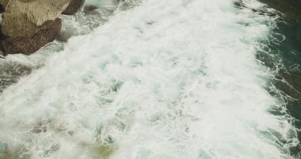 Close Up Slow Motion View of the White Sea Foam of the Ocean Waves Crashing Ashore the Rocky Beach alt