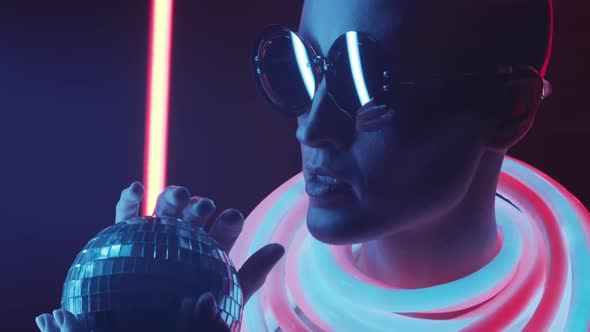 Bald Fashion Model in Trendy Glasses Posing with Disco Ball in Neon Light alt