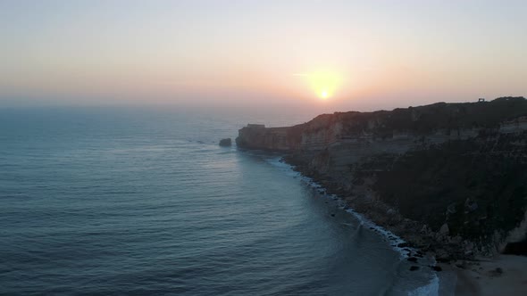 Drone shot of Cliff near wavy ocean in Nazarè Coast Village in Portugal 4K