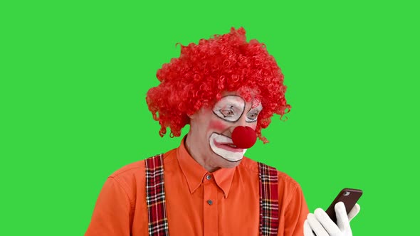 Funny Clown Looking at Smartphone and Reacting on What He Sees on a Green Screen Chroma Key alt