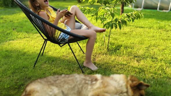 Cute kid girl playing on mobile phone and looking on the dog laying