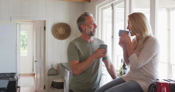 Relaxing caucasian mature couple drinking coffee and talking in kitchen alt