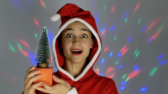 A Pretty Young Woman Dressed As Santa Claus Smiles and Holds a Little Christmas Tree in Her Hands