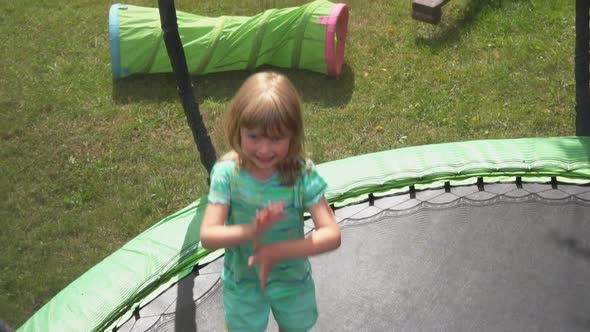 Little Cheerful Blond Girl is Jumping on the Trampoline in the Backyard alt