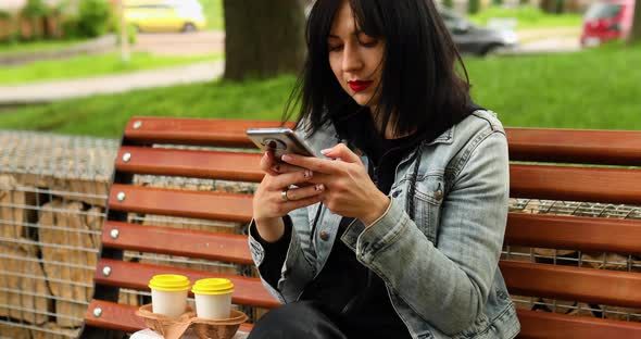 Woman sitting on the bench in the park with take away food and coffee alt
