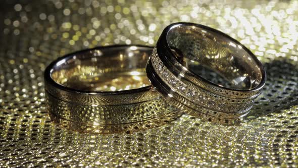 Wedding Gold Rings Lying on Shiny Glossy Surface. Shining with Light. Close-up alt