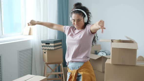 Happy Asian Girl Wearing Headphones Dancing in New House After Moving in alt