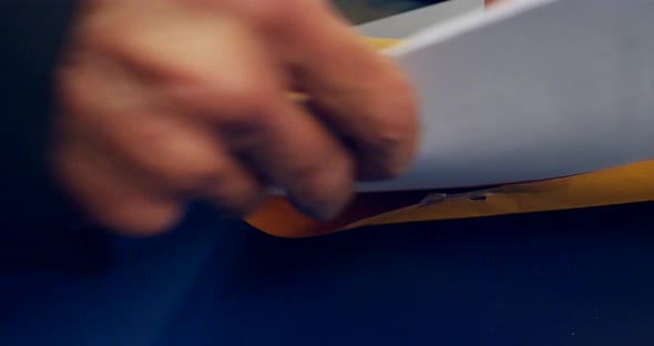 Close up on hands opening an orange envelope and placing important documents inside to be mailed and alt
