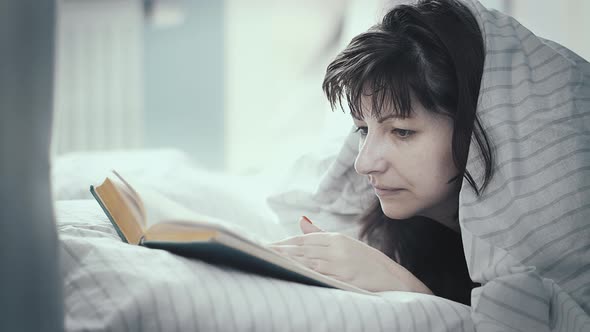 Pretty Brunette Woman Lies In Bed And Attentively Reads A Book Day Off in Bed Reading a Book