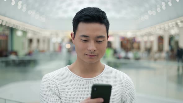 Portrait Shot of Asian Male Scrolling Phone on Big Mall Background