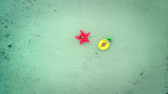 Aerial view of two girls floating on inflatable mattress in transparent sea. alt