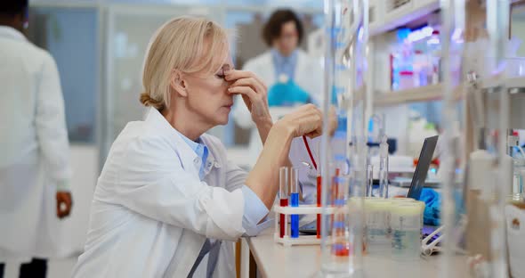 Exhausted Research Scientist Putting Off Protective Goggles Sitting at Desk in Chemical Laboratory alt